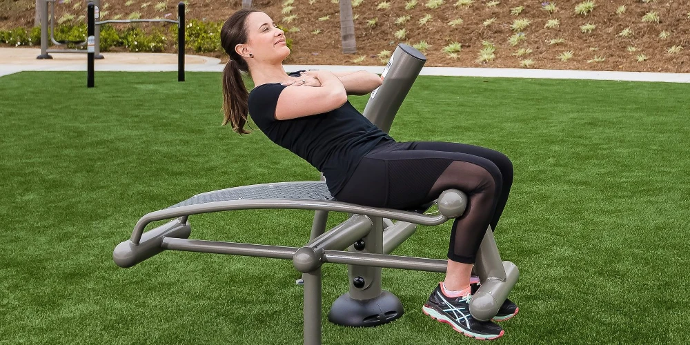 Woman performing abdominal exercises on outdoor core training bench in a park fitness area